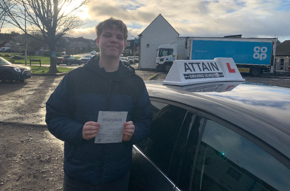 Driving Lessons Edinburgh South West - Sam Mapstone of Loanhead holding his driving test pass certificate beside the Attain Driving School car